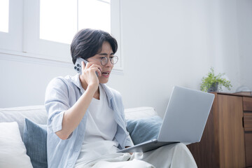 A man with glasses looking at a computer, apologizing while talking on his phone.