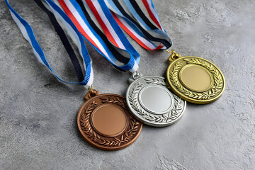 Gold, silver, and bronze medals with striped ribbons on textured gray surface
