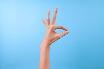 Hand Showing Ok Sign Gesture Against Light Blue Background