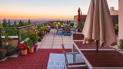 Sunset on large BC rooftop penthouse patio with deck furniture and umbrellas, with view across valley to Gulf Islands on far horizon.