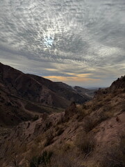 Dramatic altocumulus cloudscape over a rugged mountain valley. Scenic view of an arid canyon landscape with the sun peeking through textured clouds.