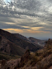 Expansive view of arid mountains under a textured, overcast sky during a golden hour sunset. A...