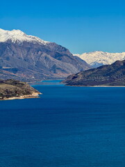 Obraz premium Vibrant blue lake surrounded by majestic snow-capped mountains. Scenic alpine landscape with clear sky. Peaceful nature background.