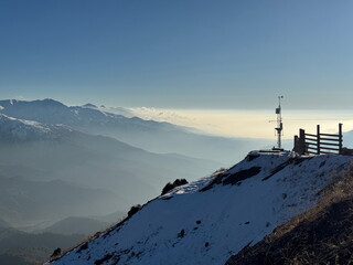 Weather station on a snowy mountain summit. Scenic view of a vast mountain range with haze in the...