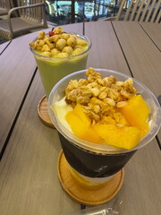 Two healthy dessert parfaits on a cafe table. A mango yogurt parfait and a green smoothie with granola and nuts.
