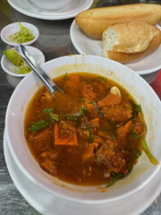A hearty bowl of traditional Vietnamese beef stew, Bo Kho, served with a fresh baguette, chili, and lime for dipping.