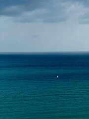 Lone sailboat on the vast open ocean. Minimalist seascape with a single boat under a cloudy sky.