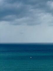 A small sailboat navigates the vast, deep blue sea under a dramatic, cloudy sky. Concept of...