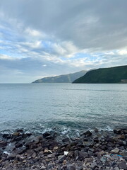 Rocky coastline with calm sea water. Mountainous landscape by the ocean under a cloudy sky. Serene...