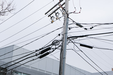 Utility pole with multiple tangled power lines against a grey sky and industrial building...