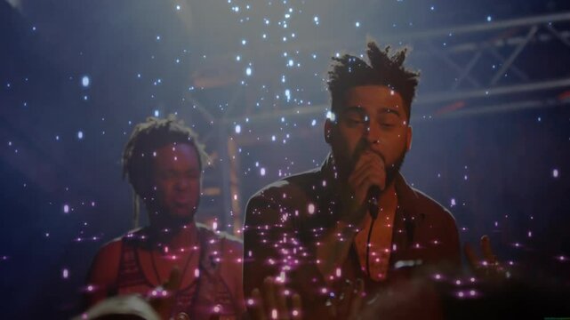 Singer raising microphone on concert stage performing song sparking particles drifting around band