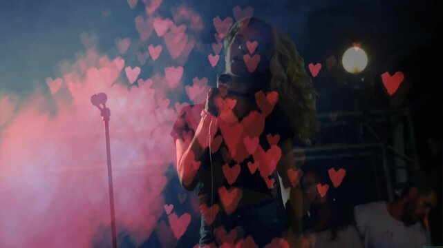 Red smoke rising, singer stepping onto stage singing into mic, hearts swirling in music performance