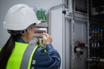 Electrician engineer performs control panel inspection wearing safety helmet and reflective vest...