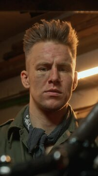 Vertical low angle shot of young man with spike hair and grase on his face repairing his bike in garage