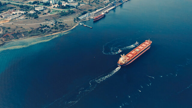 Cargo ship navigating in port harbor during daylight with surrounding vessels and coastline