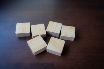 Six natural wooden blocks arranged on dark wood surface with dramatic lighting and shadow effects creating minimalist composition for crafting building and creative design concepts