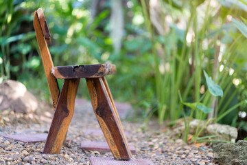 Rustic wooden chair with curved backrest placed on stone pathway in lush green garden setting with...