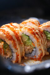Fresh sushi rolls with spicy drizzles on a dark plate
