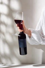 Red wine bottle and glass in bright soft lighting, minimal closeup on neutral background