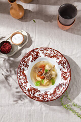 Broth with dumplings in ornate ceramic bowl, bright daylight, overhead composition