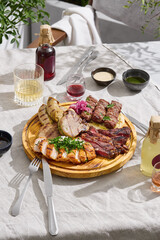 Grilled meat assortment platter in bright sunlight, overhead composition with rustic table setting