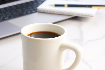 Laptop with cup of coffee and notepad with pen on desk at office
