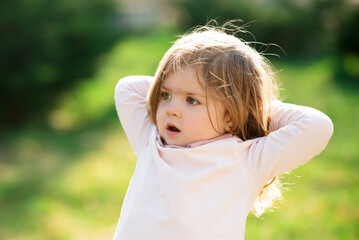 Surprised child girl playing in the green grass on summer field. Emotional baby face.