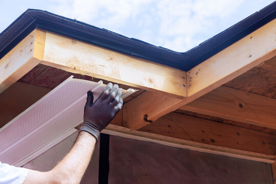 Skilled worker places plastic soffit material in eaves of house while working outdoors.