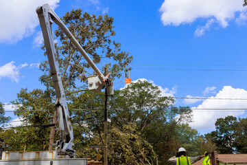 Utility workers use cherry picker to restore power lines damaged by recent storms in suburban...
