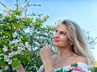 Mature blonde woman poses for a lifestyle blog selfie among blooming flowers on a sunny day