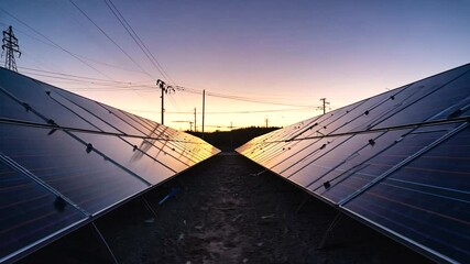 Sunset view of solar panels aligned in rows, capturing renewable energy with power lines in the background