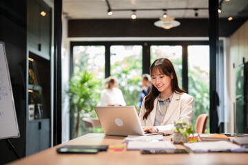 Young asian businesswoman using laptop for remote work .young woman sits at office desk , texting,...