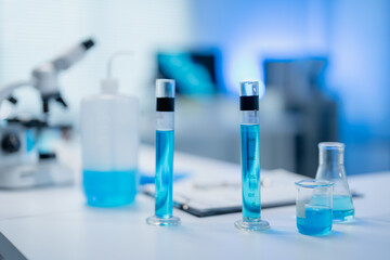 Modern laboratory setup featuring test tubes and beakers filled with blue liquid, emphasizing scientific research and experimentation. A microscope is visible in the background