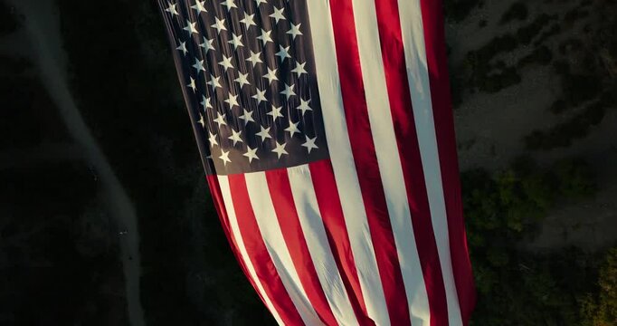 Slow spinning drone shot sinking in on glowing American flag flowing in canyon - Powered by Adobe