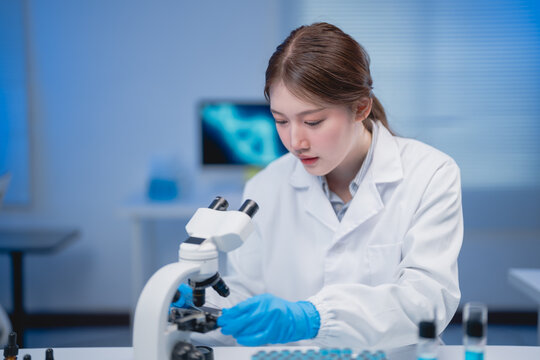 Dedicated scientist in a laboratory setting, wearing a lab coat and gloves, carefully examines samples using a microscope. The background features lab equipment and a computer screen
