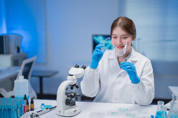 Young scientist wearing a lab coat and gloves, removing a face shield after completing work in a...