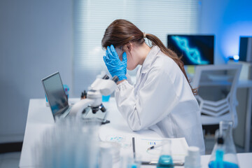 Young Asian scientist woman covering her face with hands, feeling overwhelmed and fatigued while...