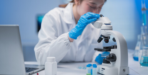 Asian female scientist wearing lab coat and gloves using microscope in laboratory doing scientific...