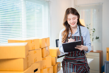 Young smiling female entrepreneur wearing an apron checking order list on clipboard while working...