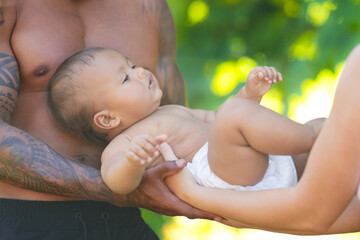 Happy baby. Close up of Biracial baby lying on parents hands. Father and Mother hug Biracial baby child. Multiracial Fathers and mothers hand for baby. Child in tender caring hands. Babies love.