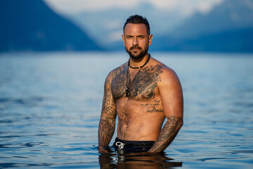 Muscular man relax in water at the lake. Sexy male model in sea water. Handsome boy rest in Alps lake water. Sexy naked wet male torso in drop water. Man freedom lifestyle. Strong muscles guy.