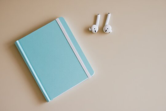 Light teal notebook and white earbuds on a beige surface.