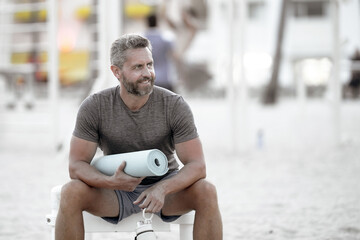 Sport man resting on a bench outdoors. Mature fitness sport model sitting on a bench after a...