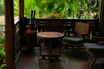 Wooden chairs and coffee table on open veranda surrounded by tropical plants