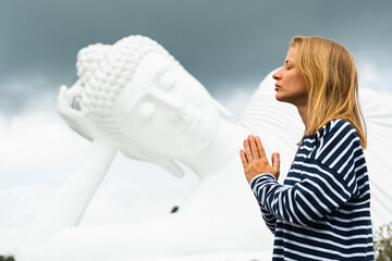
A young girl of European appearance folds her hands in namaste and meditates in front of a huge...