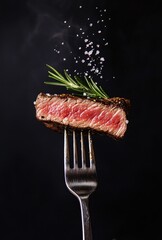 Steak on fork with rosemary and salt, cooking detail, black background