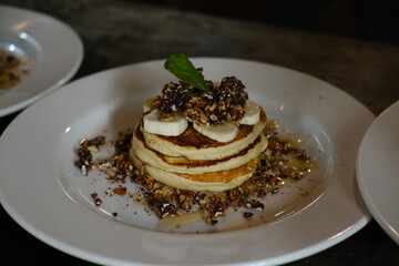 Stack of Banana Pancakes with Granola and Honey on White Plate
