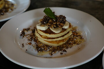 Stack of Banana Pancakes with Granola and Honey on White Plate