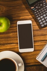 Showing desk with white smartphone alongside calculator, green apple, coffee, notebook and blue pen