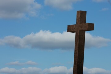 Flat design illustration showing wooden cross standing against pale blue sky dotted with clouds